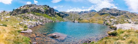 Magnifico paesaggio di ruvida catena montuosa rocciosa che circonda calmo lago blu sotto cielo azzurro nella soleggiata giornata estiva nei Pirenei Catalani — Foto stock