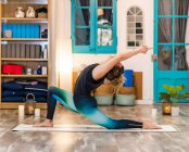 Vista lateral da mulher anônima em activewear fazendo Crescent Lunge pose enquanto pratica ioga no estúdio de luz — Fotografia de Stock