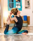 Vista lateral de una joven en ropa deportiva haciendo pose de paloma rey de una pierna mientras practica yoga en un estudio de luz - foto de stock