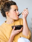 Young blonde cheerful woman in casual clothes eating healthy food from natural coconut bowl in light room — Stock Photo