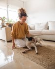 Cheerful woman with curly hair an casual clothes sitting on the floor with obedient Ratonero Bodeguero Andaluz in light apartment — Stock Photo