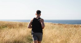 Musculoso corredor masculino corriendo a lo largo del camino en el prado durante el entrenamiento en el fondo del mar en verano - foto de stock