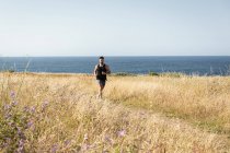Muscular male jogger running along path in meadow during training on background of sea in summer — Stock Photo