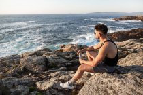 Вид збоку мирного чоловіка, що сидить на скелі на узбережжі і захоплюється спокійним морем на світанку влітку — стокове фото