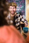 Young cheerful couple in bright casual clothes talking in cosy kitchen and looking at each other while having a coffee — Stock Photo