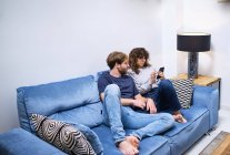 Happy young couple in casual clothes sitting on couch and embracing while spending time together — Stock Photo
