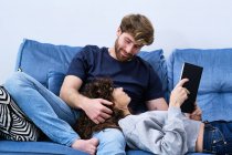 De baixo jovem mulher em roupa casual deitado no sofá e livro de leitura colocando a cabeça sobre os joelhos do namorado — Fotografia de Stock