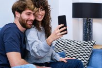Молодой бородатый мужчина близок к улыбающейся женщине в повседневной одежде, делающей селфи на мобильный телефон — стоковое фото