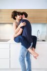 Vista lateral do jovem casal em roupas casuais abraçando suavemente na cozinha leve no balcão — Fotografia de Stock