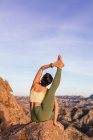 Flexible female in sportswear performing Heron pose on top of rocky hill while practicing yoga — Stock Photo