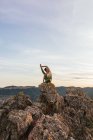 Mujer flexible en ropa deportiva realizando pose de garza en la cima de una colina rocosa mientras practica yoga - foto de stock