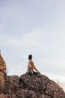 Low angle of calm unrecognizable female performing yoga exercise while practicing meditation on rocky ground at bright sunset — Stock Photo