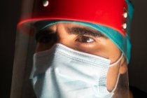 Primer plano del cirujano masculino en máscara médica mirando hacia otro lado en habitación oscura - foto de stock
