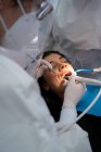 Професійний стоматолог в уніформі з медичною маскою буріння зуба спокійної жінки за допомогою помічника — стокове фото