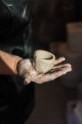 Обрізана невпізнавана доросла жінка-художниця, що стоїть у легкій студії і тримає свіжий керамічний горщик ручної роботи — стокове фото