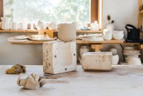 Легка студія з керамічними горщиками на поверхні біля полиці з керамічним посудом ручної роботи — стокове фото