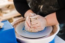 Crop anonymous female artisan in apron modeling clay pot on throwing wheel - foto de stock