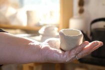 Cropped unrecognizable adult female artisan standing in light studio and holding fresh handmade ceramic pot — Fotografia de Stock
