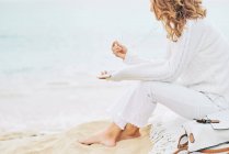 Вид збоку спокійна жінка сидить на пляжі біля моря і насолоджується музикою на навушниках та використовує мобільний — стокове фото