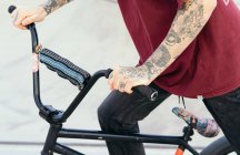 Side view of crop anonymous hipster male biker riding BMX bicycle in skate park in daytime - foto de stock