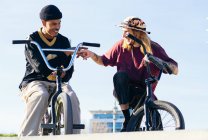 From below of young cheerful multiethnic sportsmen on trial bicycles looking at each other during greeting in city — Stock Photo