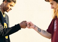 Side view of crop young multiracial hipster men in cool outfit with piercings and tattoos greeting each other on light background — Stock Photo