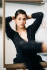 Junge nachdenkliche Frau in schwarzer Kleidung und Ohrring blickt in die Kamera im Spiegel auf Staffelei gestellt — Stockfoto