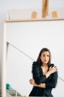 Young pensive female in black wear and earring looking at camera in mirror placed on easel — Stock Photo