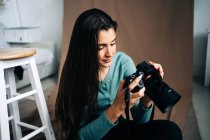 Millennial fêmea com câmera de foto profissional sentado no fundo têxtil castanho amassado em casa — Fotografia de Stock