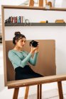 Giovane donna in abito casual con macchina fotografica digitale professionale che riflette nello specchio in casa — Foto stock