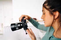Тысячелетняя самка с профессиональной фотокамерой сидит дома на светлом фоне — стоковое фото