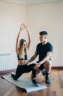 Corpo completo di istruttore personale maschile sostenere donna facendo affondi esercizio con le braccia sollevate sul tappeto durante l'allenamento a casa — Foto stock