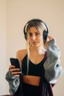 Fit feminino em fones de ouvido ouvindo música e surfando celular após o treino em casa — Fotografia de Stock