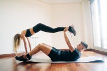 Ganzkörper-Seitenansicht eines entschlossenen Mannes und einer entschlossenen Frau in sportlicher Kleidung, die schwierige Yogapositionen ausführen, während sie zu Hause üben — Stockfoto