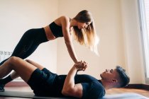 Повний вид на бік тіла визначеного чоловіка і жінки в спортивному одязі, що виконує складну позицію йоги під час тренування вдома — стокове фото