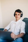 Konzentrierter Mann mit Kopfhörer hört Musik und surft modernes Netbook, während er zu Hause auf der Couch sitzt — Stockfoto