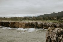 Picturesque landscape of rocky cliff near waving sea under cloudy sky on overcast day — Stock Photo