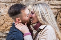 Side view of content couple gently kissing on city street against stone wall while enjoying weekend together — Stock Photo