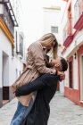 Vista lateral do conteúdo namorado levantando namorada enquanto em pé na rua da cidade perto da cidade velha olhando um para o outro — Fotografia de Stock