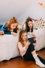 Nette kleine Mädchen spielen Spiele auf dem Tablet und ruhen sich auf weichem Bett aus, während sie das Wochenende zusammen verbringen — Stockfoto