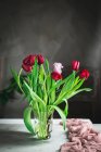 Jarrón de cristal con tulipanes rojos en la mesa junto a la ventana - foto de stock