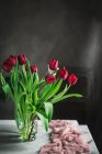 Vase en verre avec des tulipes rouges sur la table près de la fenêtre — Photo de stock