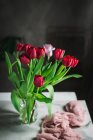 Vaso de vidro com tulipas vermelhas na mesa pela janela — Fotografia de Stock