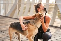 Frau in Sportbekleidung umarmt Schäferhund an der Leine beim Lauftraining am Tag — Stockfoto