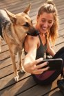 From above of smiling woman sitting near German Shepherd dog during break in running training and taking self portrait on mobile phone — Stock Photo