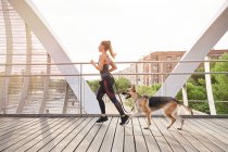 Side view full body of active female athlete running with German Shepherd dog during cardio training — Stock Photo