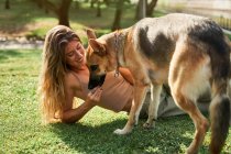 Vista lateral do proprietário fêmea positivo sentado perto do cão pastor alemão dando pata enquanto os comandos de treinamento no parque — Fotografia de Stock