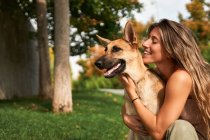 Позитивна жінка - власник обіймає німецького пса Шепарда, сидячи разом на газоні в парку. — стокове фото