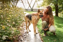 Propriétaire féminine positive embrassant chien berger allemand tout en étant assis ensemble sur la pelouse dans le parc — Photo de stock