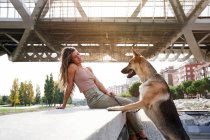 Vista lateral do proprietário feminino alegre inclinando-se com cão pastor alemão na fronteira no dique — Fotografia de Stock